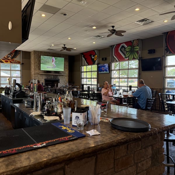 A casual restaurant interior with a stone bar, patrons dining, and sports playing on multiple TVs.